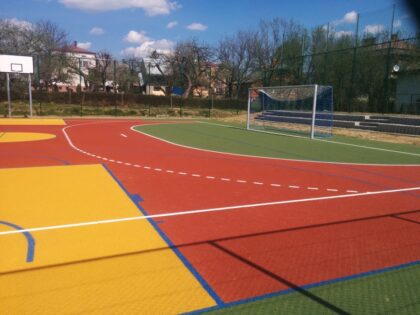 Kolorowe boisko sportowe z bramką i koszem, na zewnątrz.