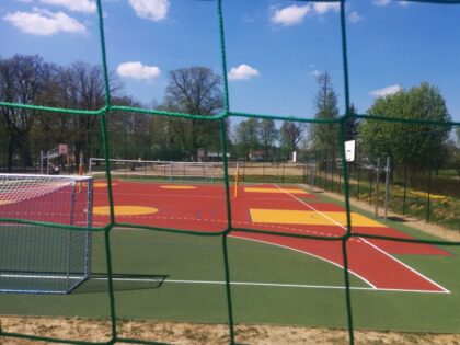 Kolorowe boisko sportowe za siatką, z bramką i koszami na zewnątrz