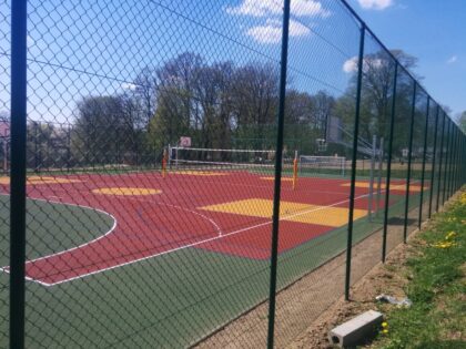 Ogrodzone wielofunkcyjne boisko sportowe z siatką i koszem, w parku.